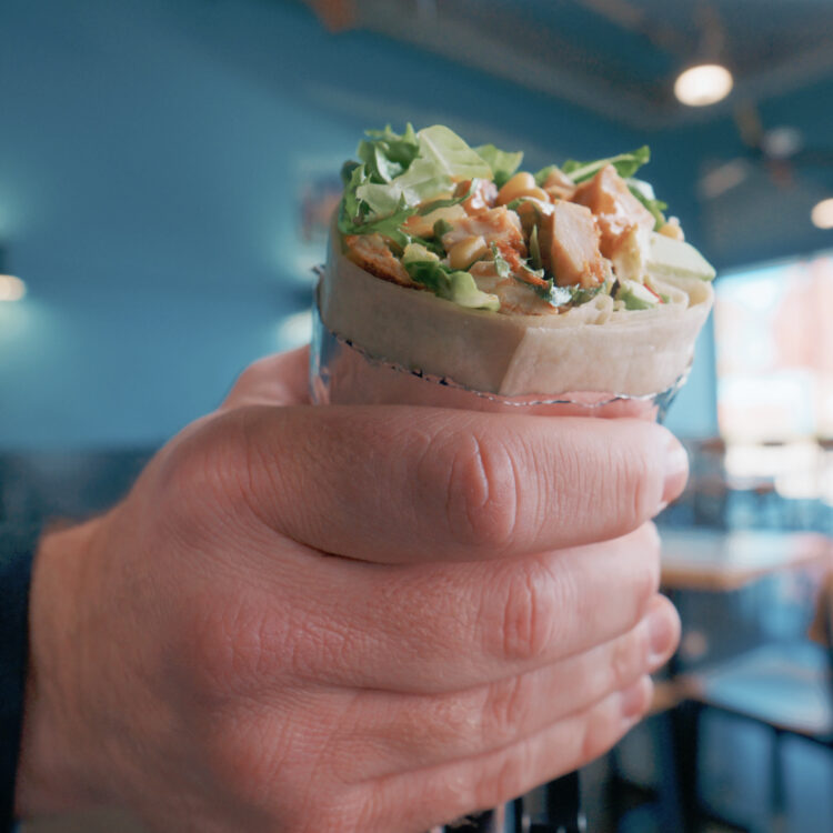 Freebirds Agave Adobo burrito held in hand inside restaurant
