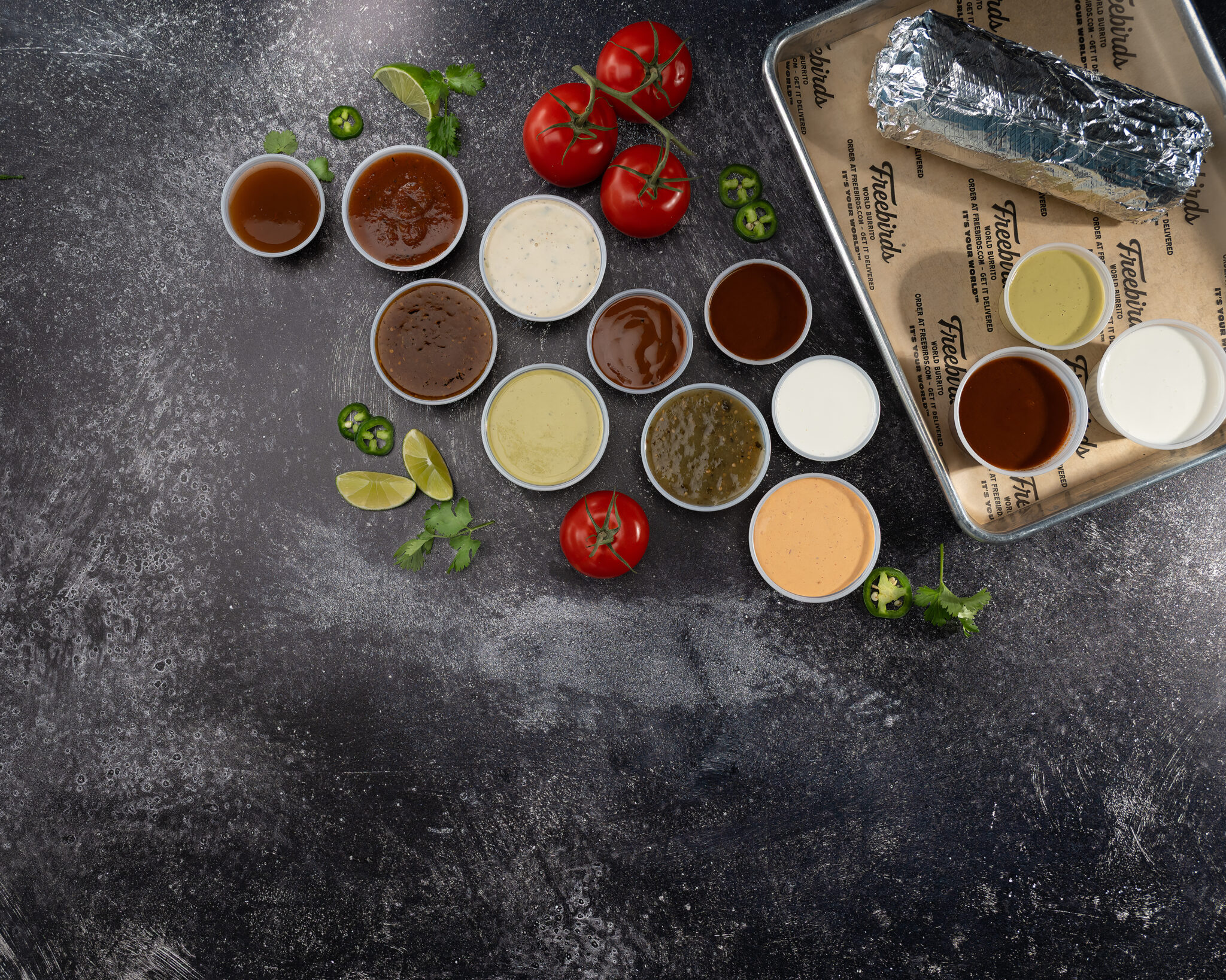 Overhead Freebirds sauce lineup with burrito, tomatoes, jalapeños, limes, and cilantro