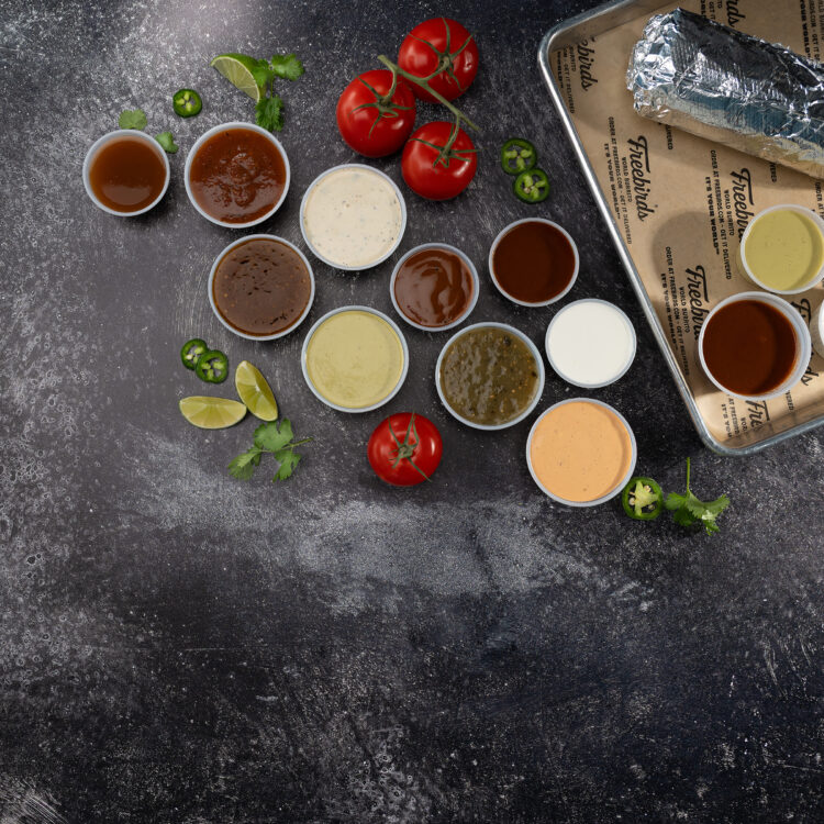 Overhead Freebirds sauce lineup with burrito, tomatoes, jalapeños, limes, and cilantro