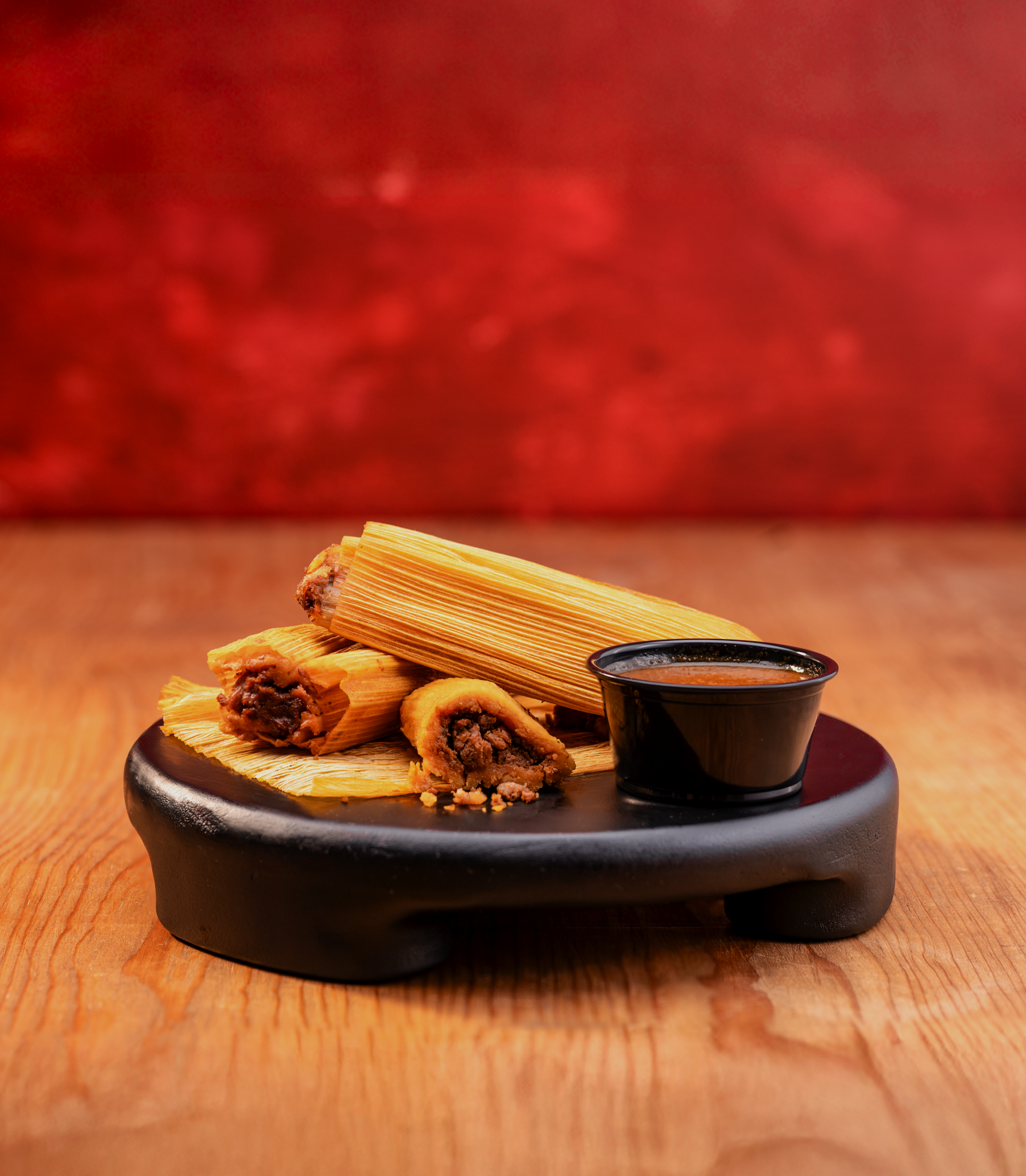 Taco Bueno pork tamales with chili sauce on black serving board