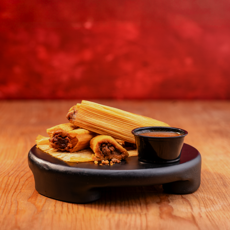 Taco Bueno pork tamales with chili sauce on black serving board